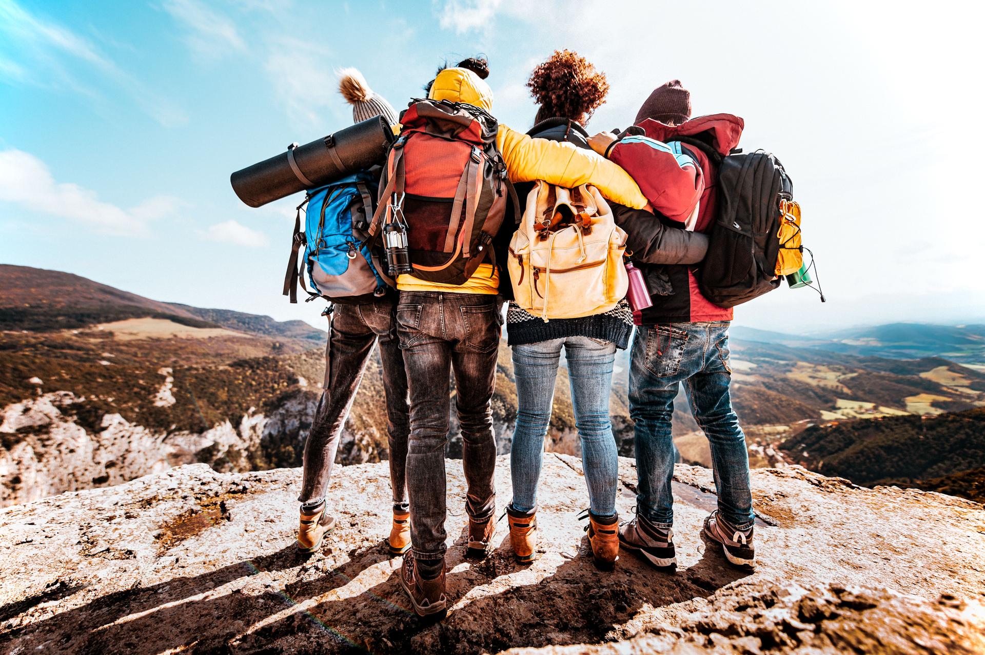 Group of tourists with backpack at sunset on the top of the mountain - Young people on a hiking trip celebrate reaching the summit - Hikers climbing and active travel vacations lifestyle concept