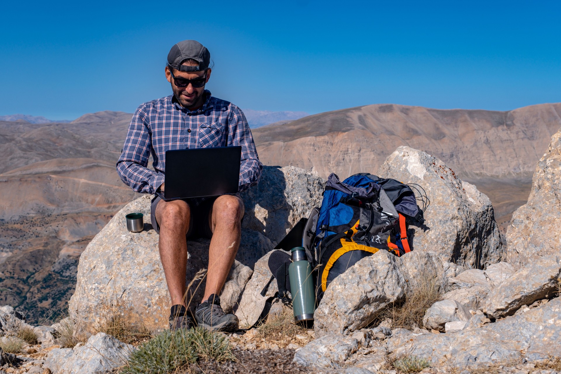 Man using laptop with backpack in mountainous area at high altitude