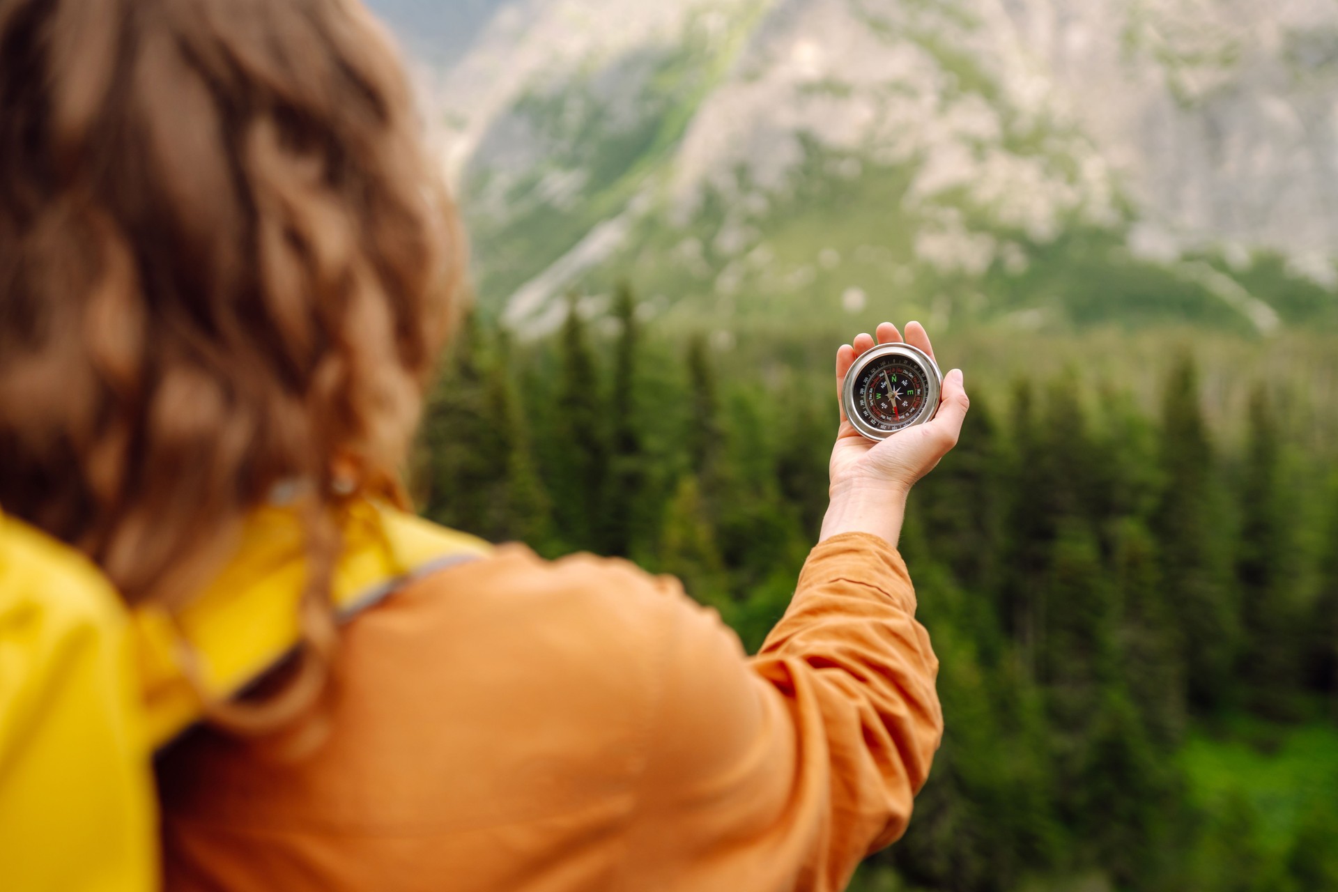 Stylish woman holding a compass in her hand while traveling in the mountains.